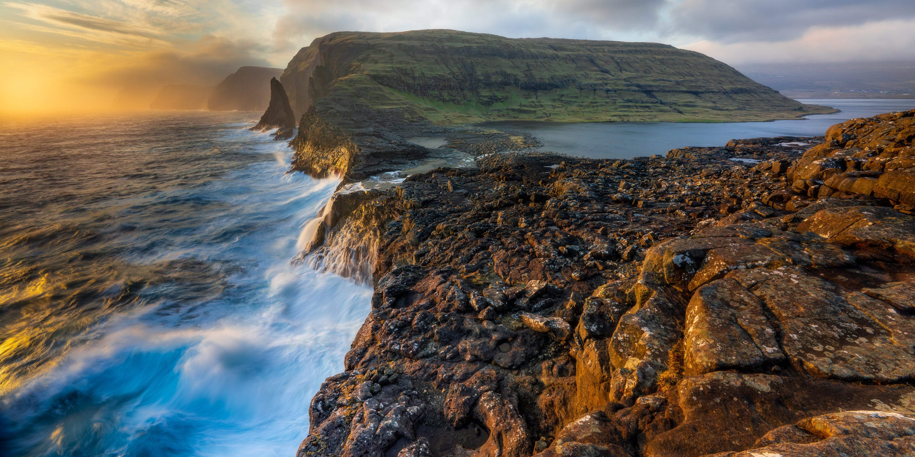 Rugged coastline with waves crashing against rocks during sunset.