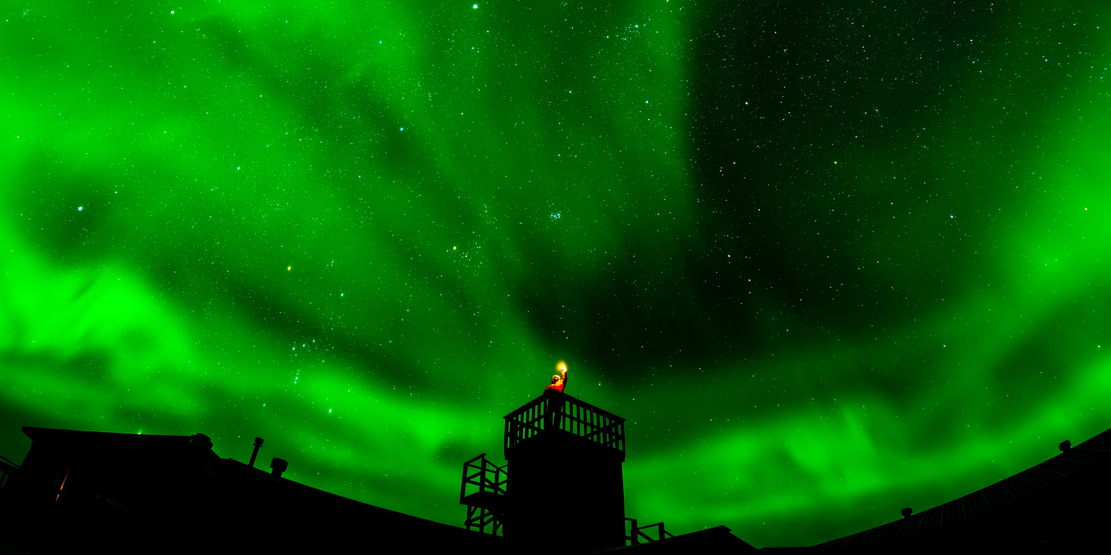 Aurora borealis over a silhouette of a town with a lighthouse.